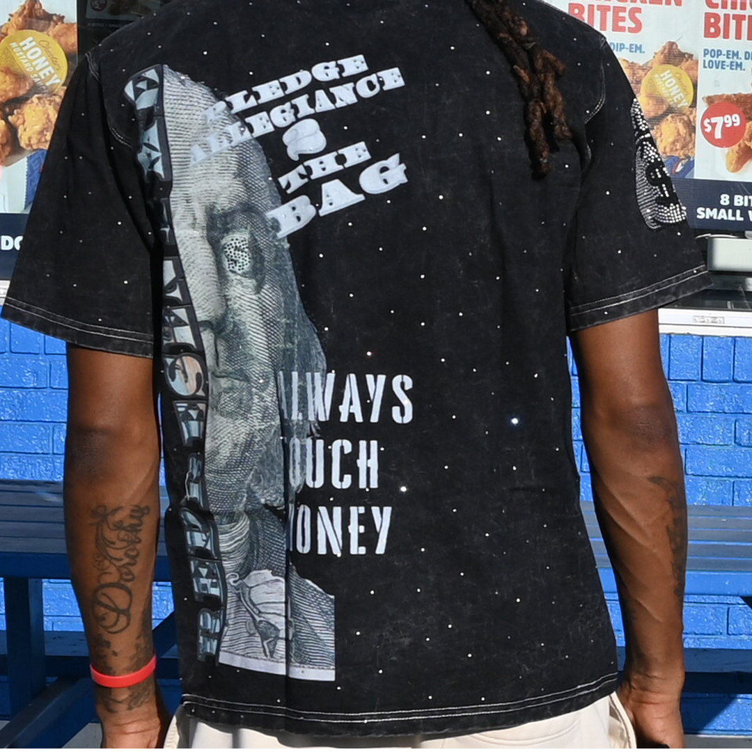 Person wearing a black t-shirt with white text and graphics, standing in front of a store with food items displayed.
